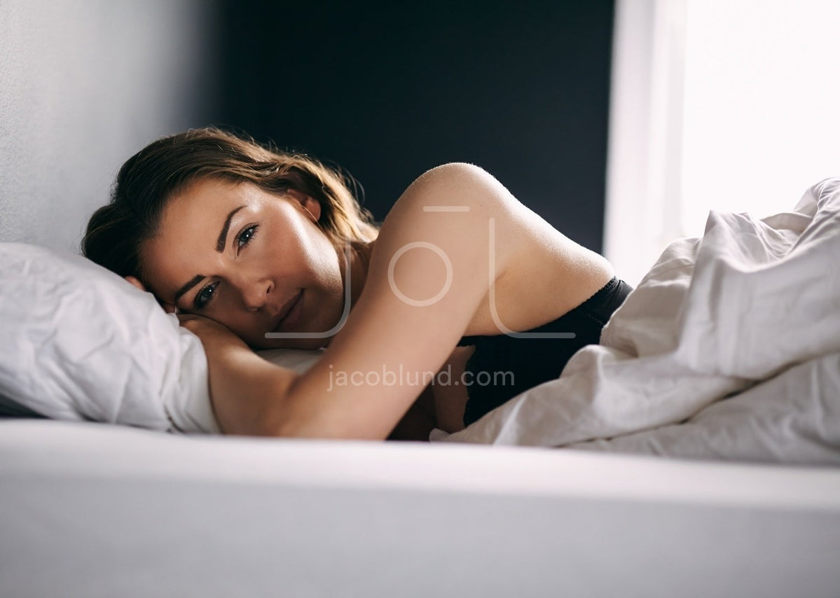 Daydreaming young woman in underwear lying on bed stock photo - OFFSET