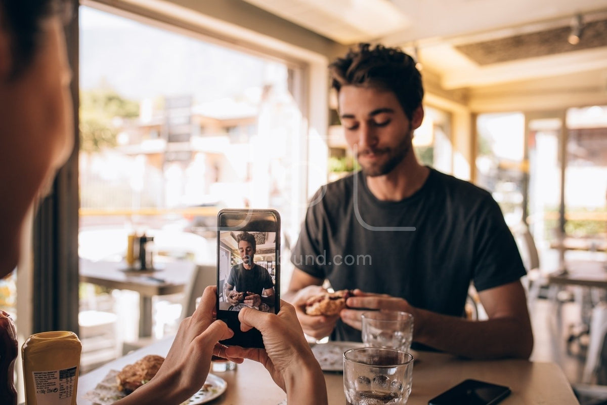 Woman capturing pictures of man eating burger – Jacob Lund Photography  Store- premium stock photo