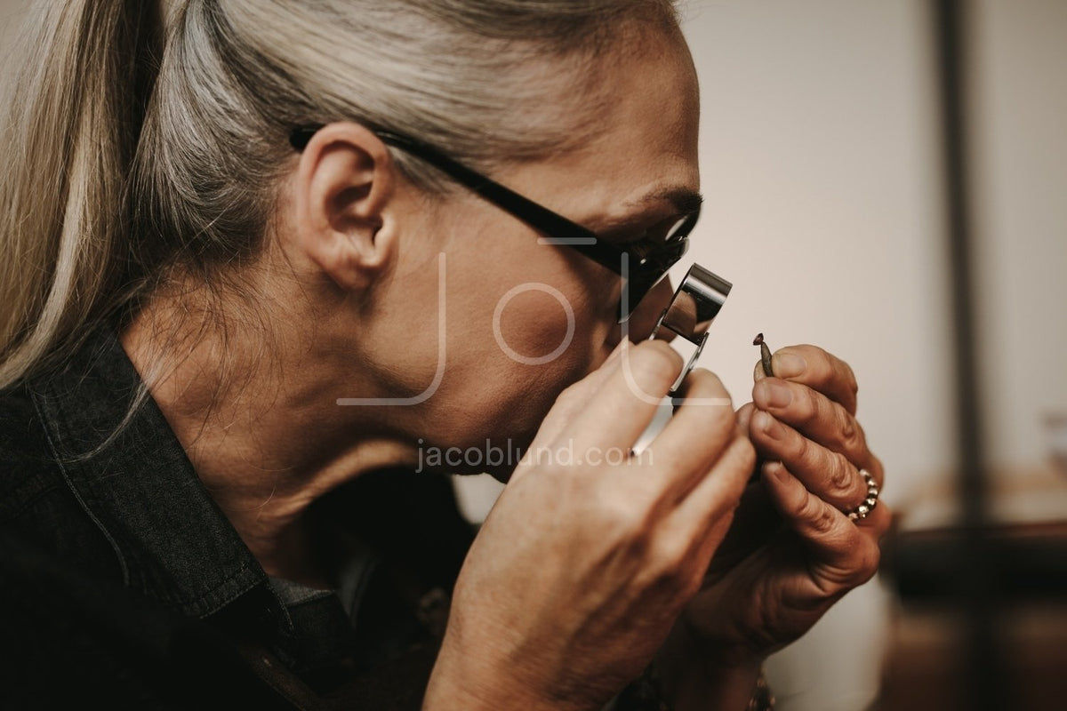 Senior jeweler examining a ring with magnifying glass stock photo